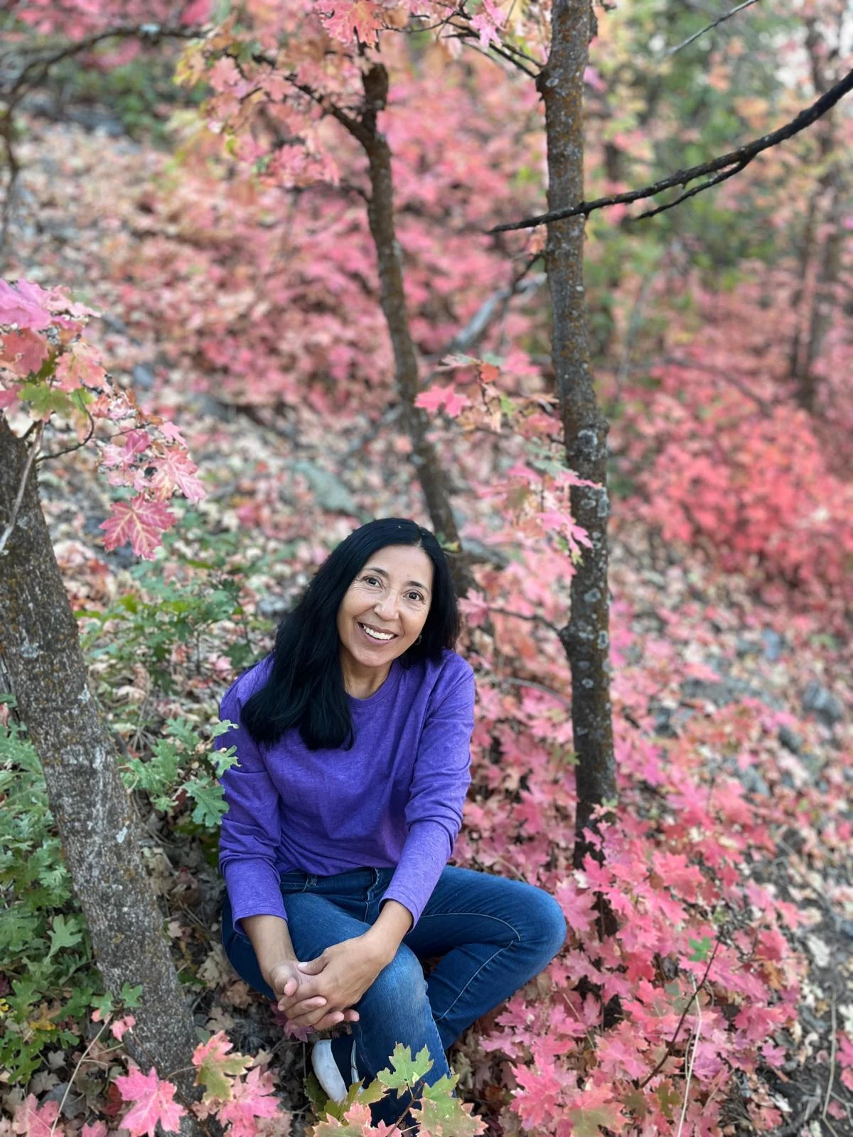 Nancy sentada en un entorno natural de árboles y hojas rosadas